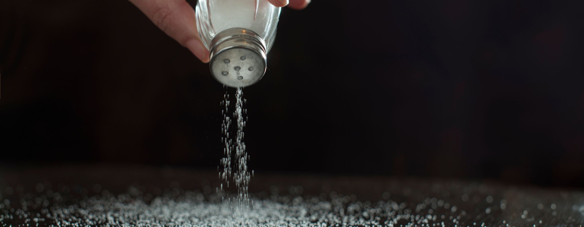 Dedos sujetando un salero con sal cayendo para ilustrar la necesidad de reducir el consumo de sal.